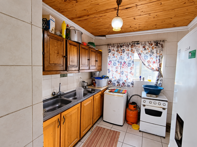 A compact kitchen featuring wooden cabinetry, a double stainless steel sink, tiled splashbacks, and a timber ceiling, offering potential for a modern renovation.