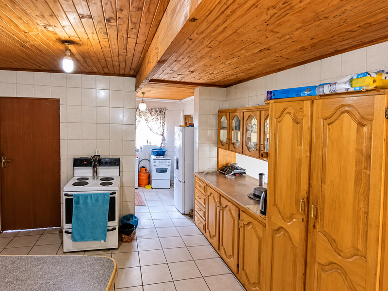 A functional kitchen featuring tiled walls, wooden cabinetry, and a distinctive tongue and groove timber ceiling, offering potential for a modern renovation.