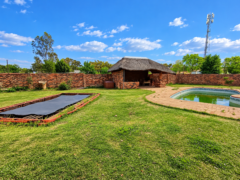 Spacious backyard featuring a swimming pool, a traditional thatched lapa, and a brick boundary wall, offering potential for outdoor entertainment.
