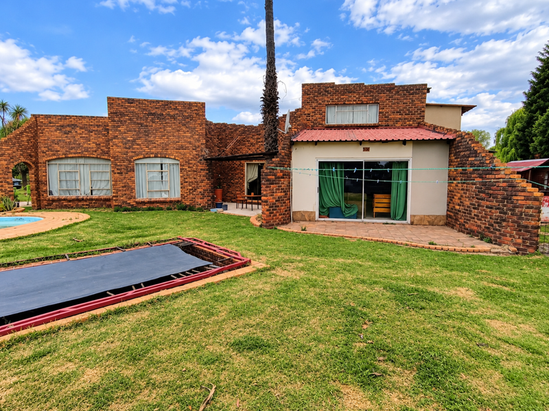Rear view of a face brick house featuring a swimming pool, paved patio area, and sliding glass doors leading to the interior.