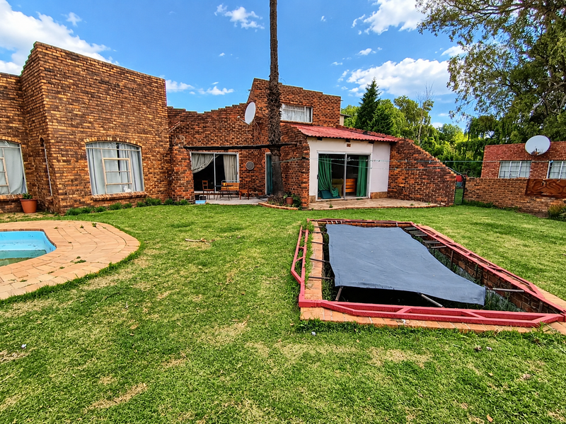 Rear view of a brick house featuring a swimming pool, in-ground trampoline, and paved patio area with sliding door access to the interior.