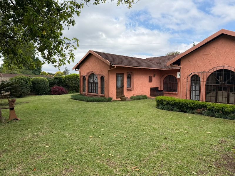 A well-maintained cottage exterior featuring a textured facade, arched windows with security bars, and a spacious, manicured rear garden.