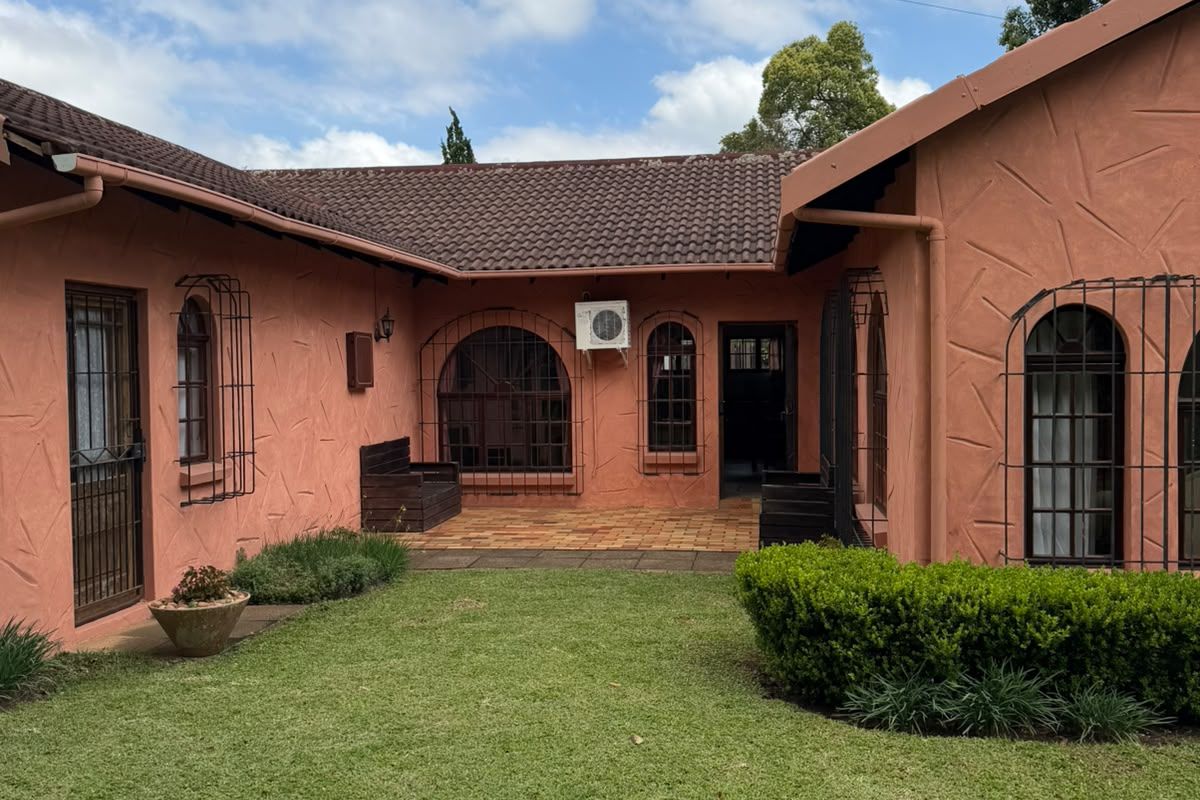 Rear view of a cottage featuring a textured stucco facade, tiled roof, security-barred windows, a paved patio area, and a well-maintained lawn.