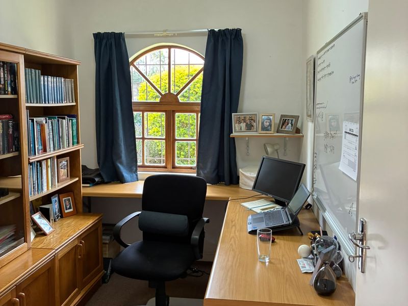 A functional home office featuring built-in wooden cabinetry, a spacious desk area, and a distinctive arched timber window providing natural light.