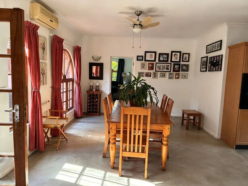 A dining room featuring concrete flooring, a ceiling fan, and an arched timber window, providing a functional space for family meals.