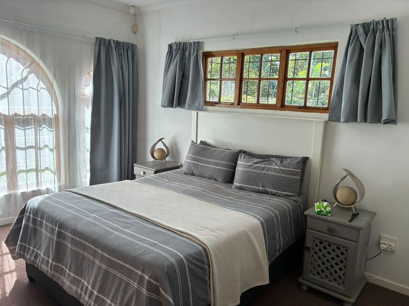 A cozy bedroom featuring timber-framed casement windows and an arched window, providing natural light and a view of the garden.