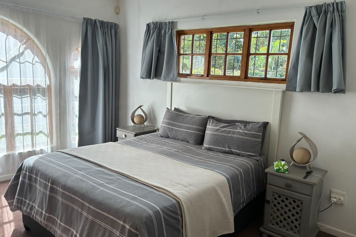 A cozy bedroom featuring timber-framed casement windows and an arched window, providing natural light and a view of the garden.