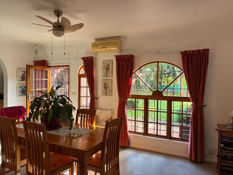 Dining area featuring arched timber-framed windows, concrete flooring, ceiling fan, and wall-mounted air conditioning unit with direct access to the garden.