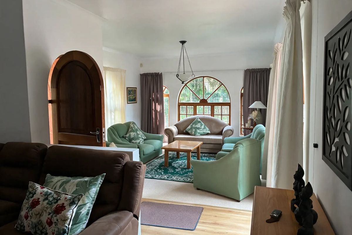 A spacious living room featuring an arched wooden door, distinctive arched windows, and laminate flooring, offering a bright and inviting atmosphere.