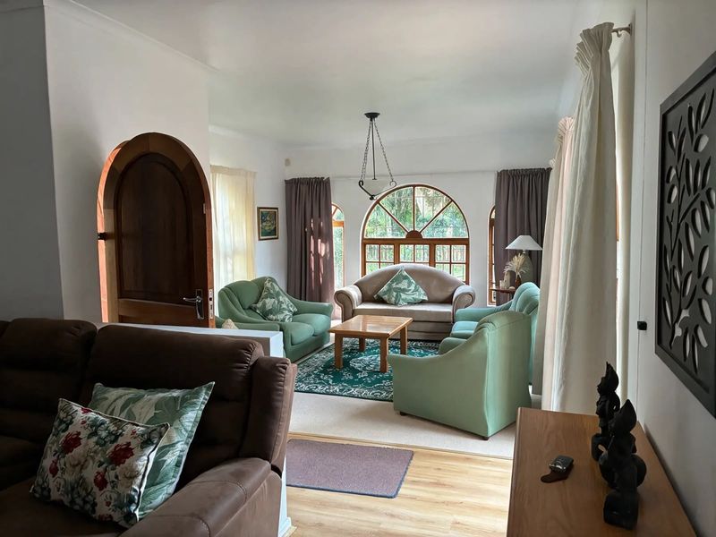 A spacious living room featuring an arched wooden door, distinctive arched windows, and laminate flooring, offering a bright and inviting atmosphere.