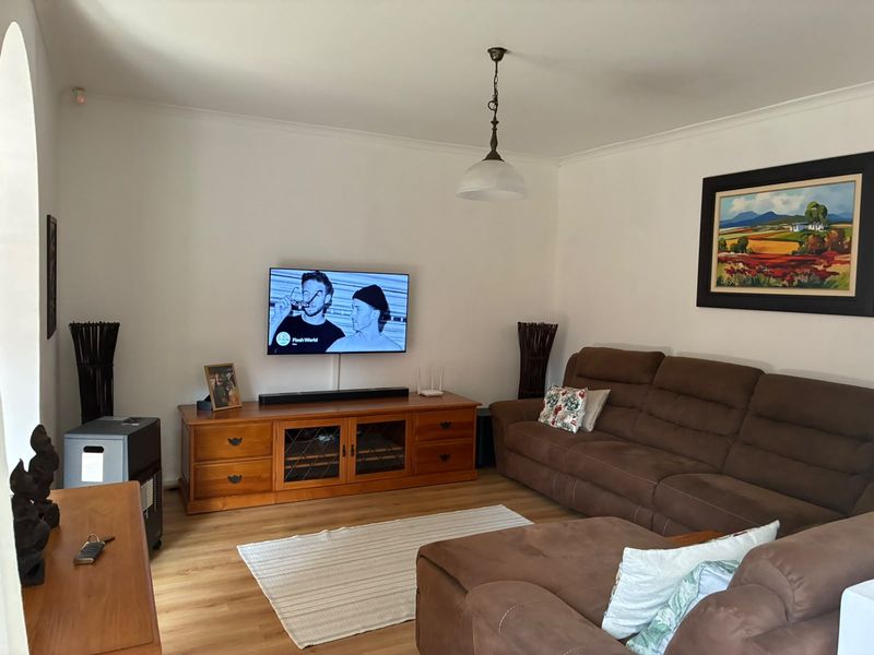 A comfortable living room featuring laminate flooring, neutral walls, and a classic pendant light fixture, providing a functional and inviting space.