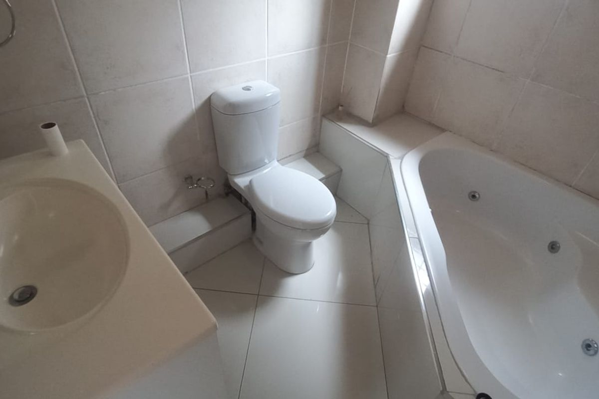 A functional bathroom featuring a built-in vanity with basin, a standard toilet, and a corner spa bath with tiled finishes throughout.