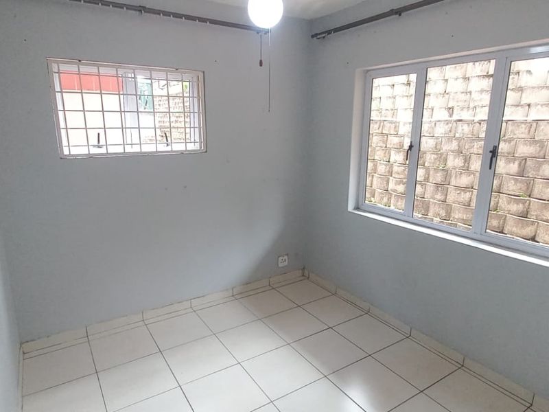 A vacant bedroom featuring tiled flooring, aluminium window frames, and security bars, offering a blank canvas for potential interior design updates.