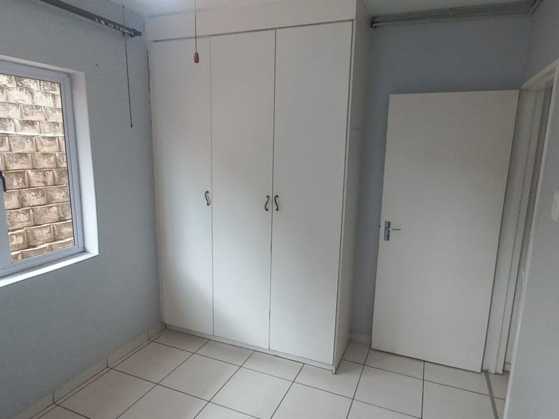 A clean, empty bedroom featuring tiled flooring, a built-in wardrobe, and an aluminium-framed window overlooking a retaining wall.