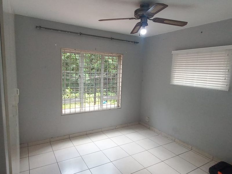 An empty bedroom featuring tiled flooring, a ceiling fan, built-in wardrobe, and security bars on the window.