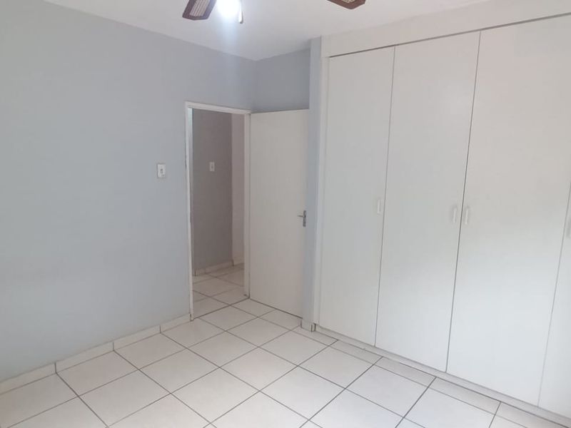 A clean, empty bedroom featuring neutral tiled flooring, light grey walls, and ample built-in cupboard storage space.