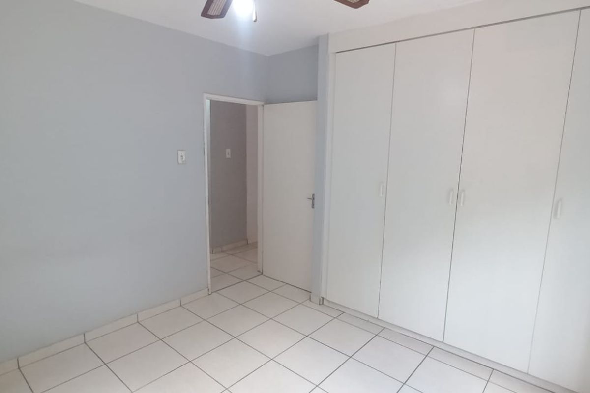 A clean, empty bedroom featuring neutral tiled flooring, light grey walls, and ample built-in cupboard storage space.