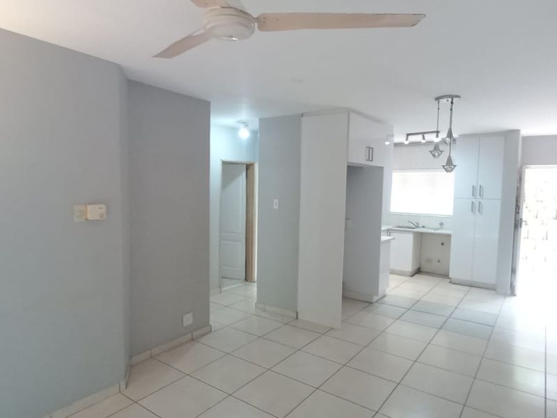 An open-plan living and kitchen area featuring neutral tiled flooring, built-in cabinetry, and modern lighting fixtures in a clean, vacant space.