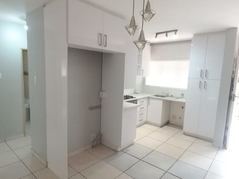 A bright, modern kitchen featuring white built-in cabinetry, tiled flooring, and integrated appliances, offering a clean and functional space.