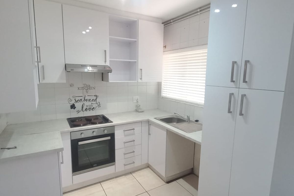 A clean, modern kitchen featuring white cabinetry, built-in oven and hob, stainless steel sink, and tiled flooring with ample storage space.