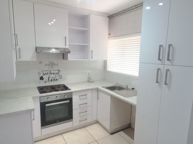 A clean, modern kitchen featuring white cabinetry, built-in oven and hob, stainless steel sink, and tiled flooring with ample storage space.
