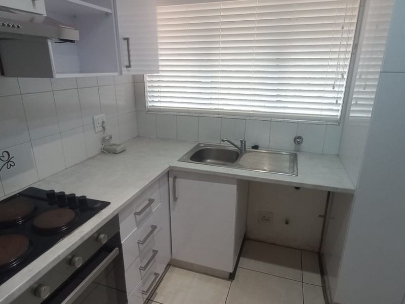A clean, functional kitchen featuring white cabinetry, laminate countertops, a built-in oven with hob, extractor fan, and a stainless steel sink.