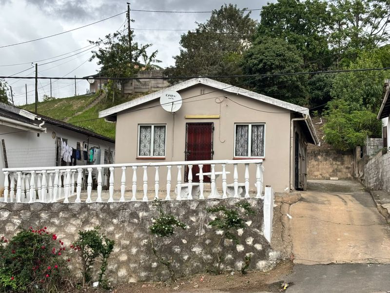 Front view of a detached house featuring a stone retaining wall, a concrete driveway, and a front patio area with a balustrade.