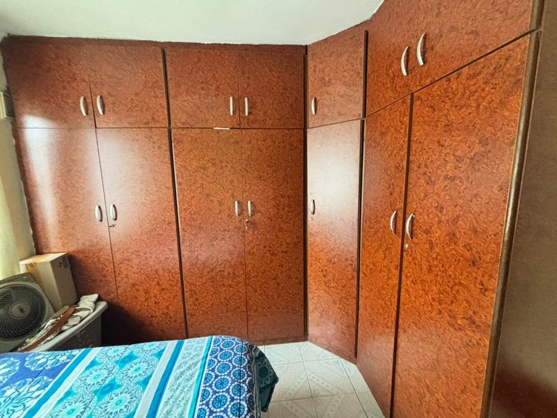 A bedroom featuring extensive floor-to-ceiling built-in wooden cupboards and tiled flooring.