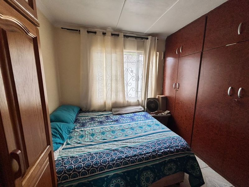 A functional bedroom featuring built-in wooden cupboards, tiled flooring, and a window fitted with a security gate.