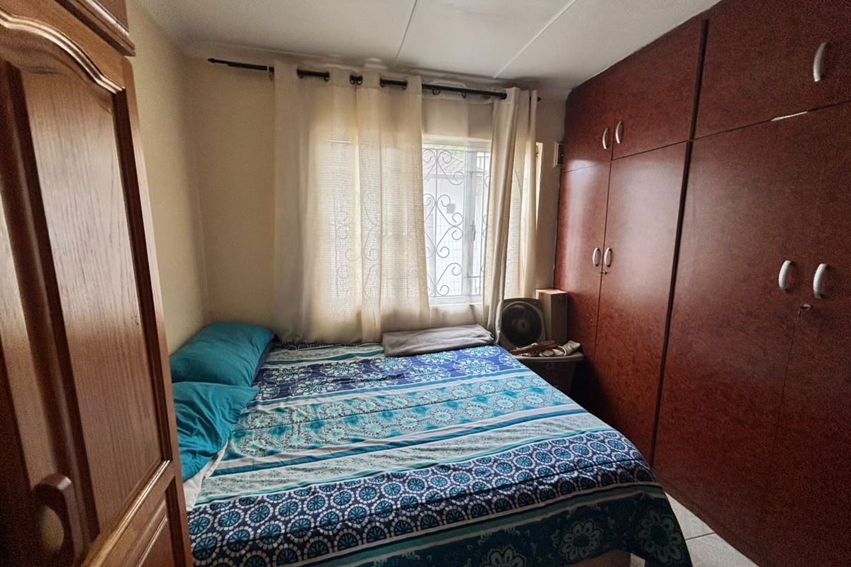 A functional bedroom featuring built-in wooden cupboards, tiled flooring, and a window fitted with a security gate.