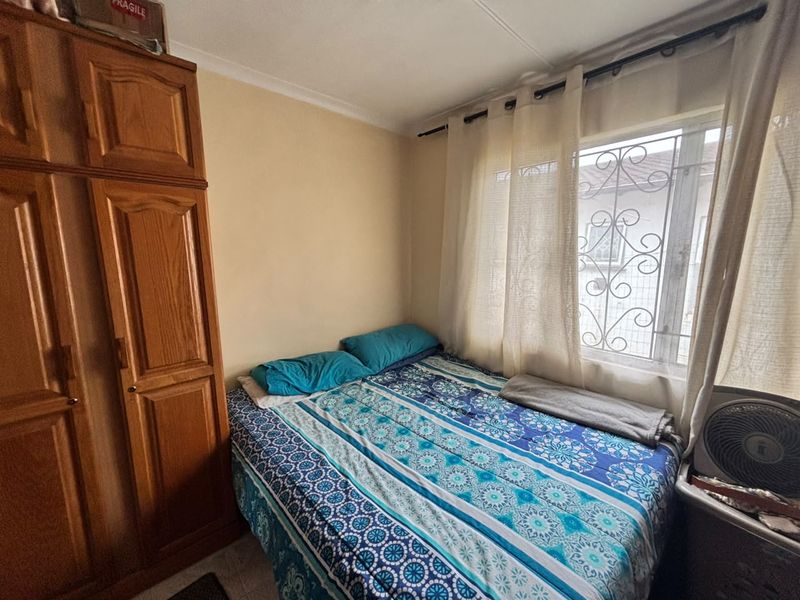 A compact bedroom featuring a built-in wooden wardrobe and a window fitted with a decorative security gate.