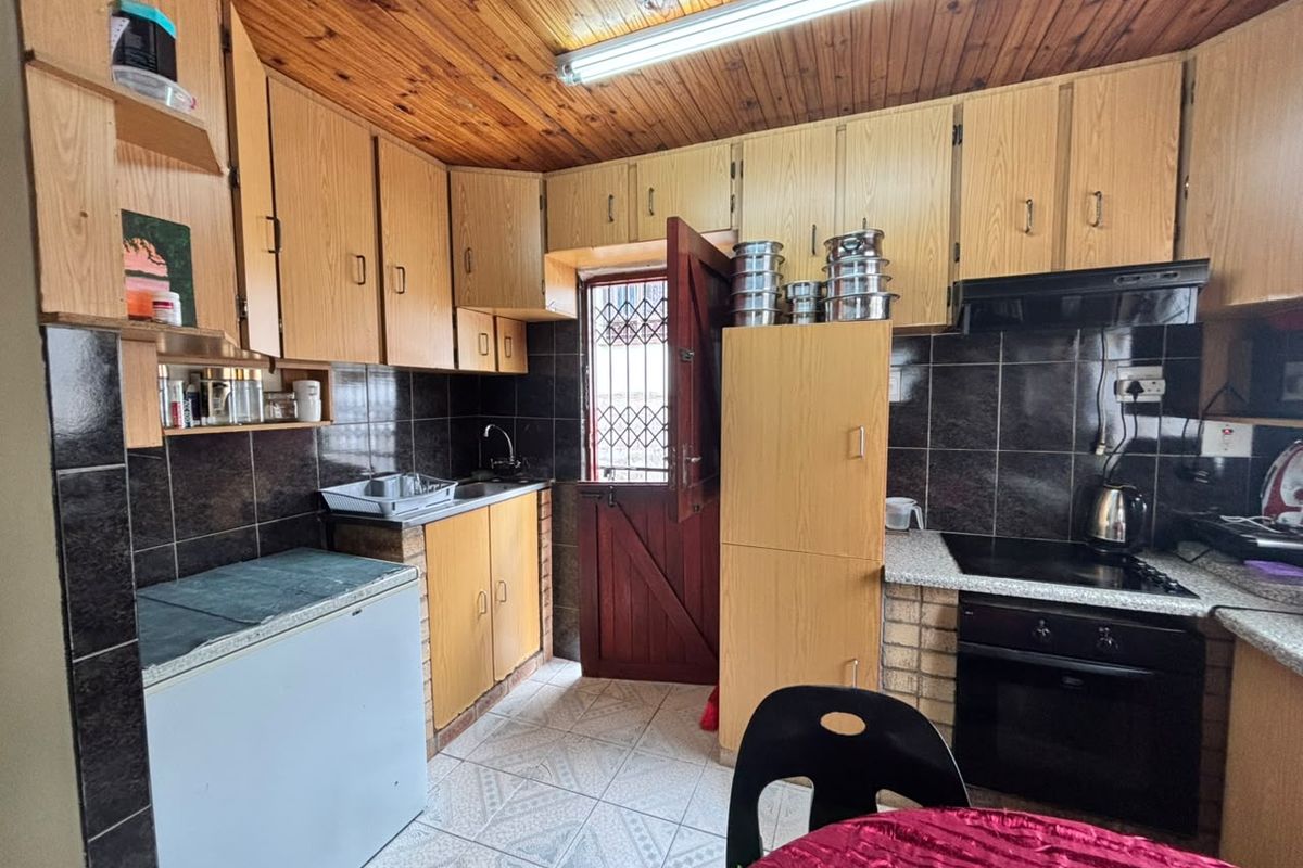 A functional kitchen featuring wooden cabinetry, tiled backsplash, built-in oven with hob, and a timber ceiling, providing a classic layout with direct exterior access.