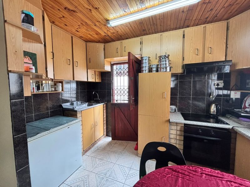 A functional kitchen featuring wooden cabinetry, tiled backsplash, built-in oven with hob, and a timber ceiling, providing a classic layout with direct exterior access.
