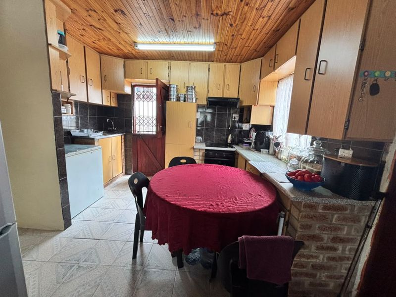 A dated kitchen featuring wooden ceiling panels, laminate cabinetry, tiled backsplash, and a brick-base breakfast counter with integrated oven and extractor fan.