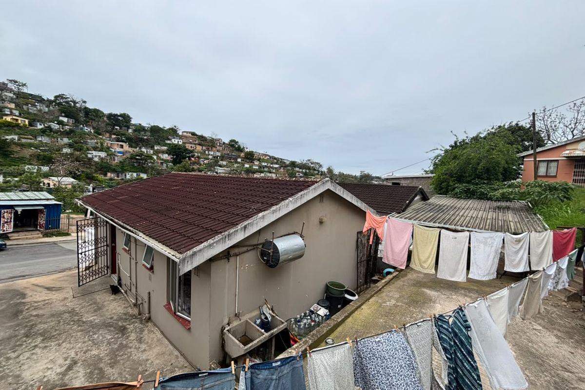Rear exterior view of the property featuring a tiled roof, external geyser, concrete wash basin, and paved yard area.