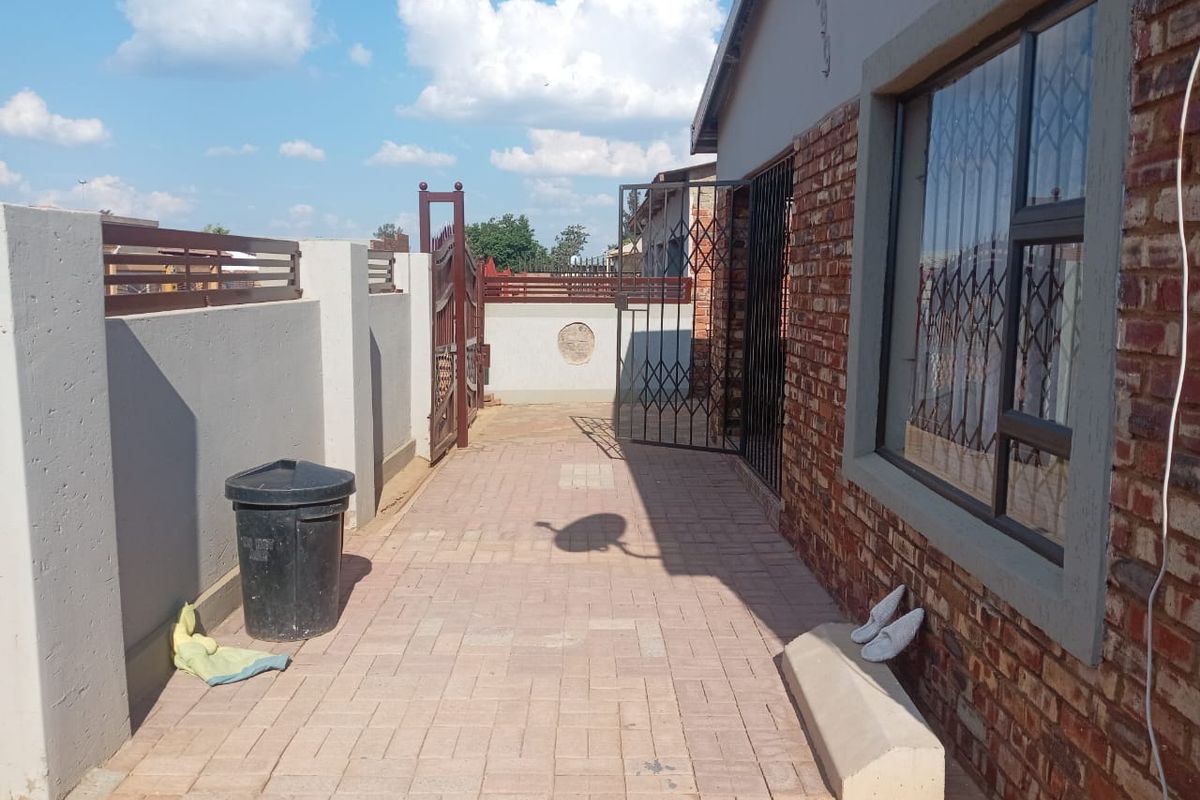 A paved side walkway featuring a brick exterior wall, security gates, and perimeter walling.