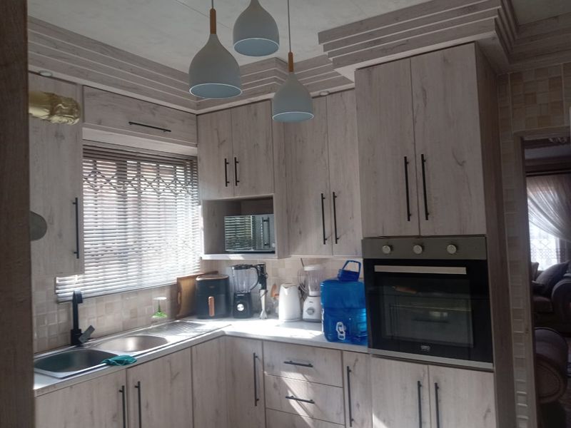 A functional kitchen featuring light wood-grain cabinetry, integrated oven and microwave, stainless steel sink, and tiled backsplash with natural light from the window.