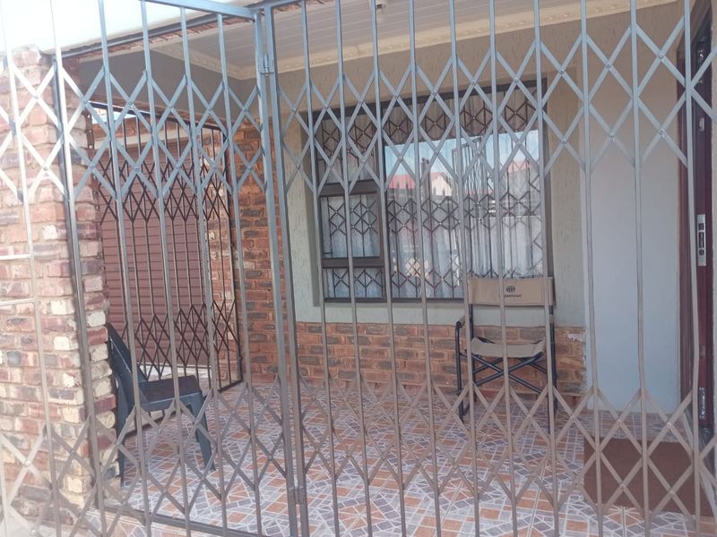 A covered patio area featuring face brick walls, tiled flooring, and full security gate enclosure.