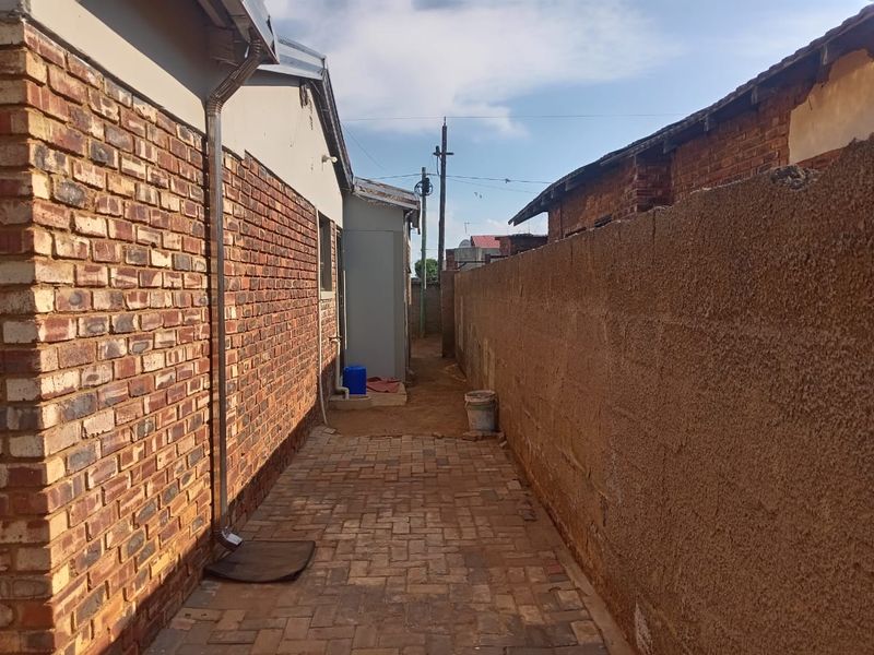 A narrow side passage featuring brick paving, a downpipe, and a high boundary wall separating the property from the adjacent lot.
