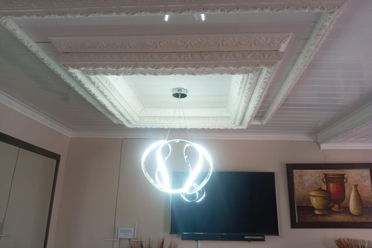 A living room interior featuring a detailed, ornate coffered ceiling with decorative molding and a modern pendant light fixture.
