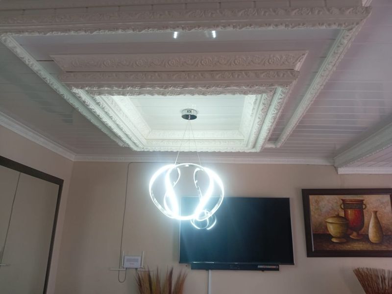 A living room interior featuring a detailed, ornate coffered ceiling with decorative molding and a modern pendant light fixture.