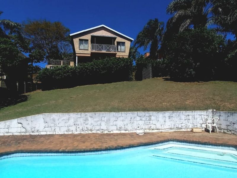 Rear view of the property featuring a swimming pool, paved surround, and a raised brick retaining wall leading to the main house and balcony.