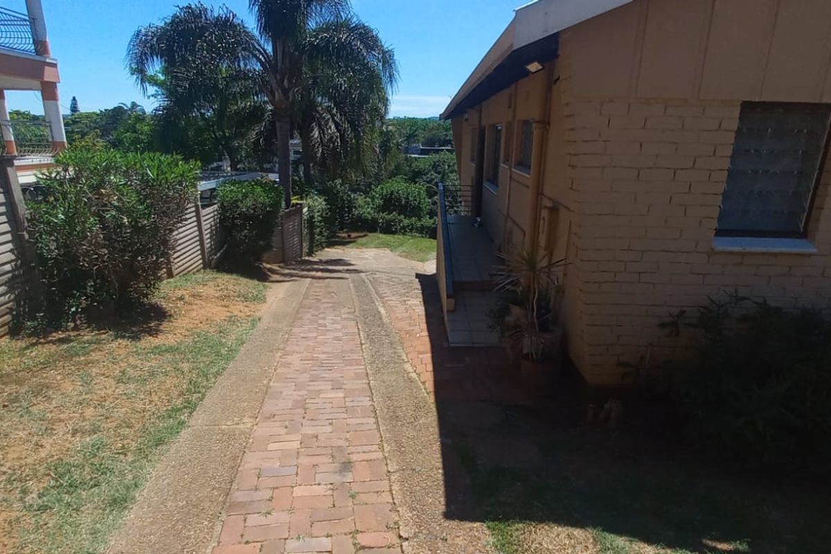 Rear exterior view showing a brick paved driveway, side access path, and brick building facade with security fencing.