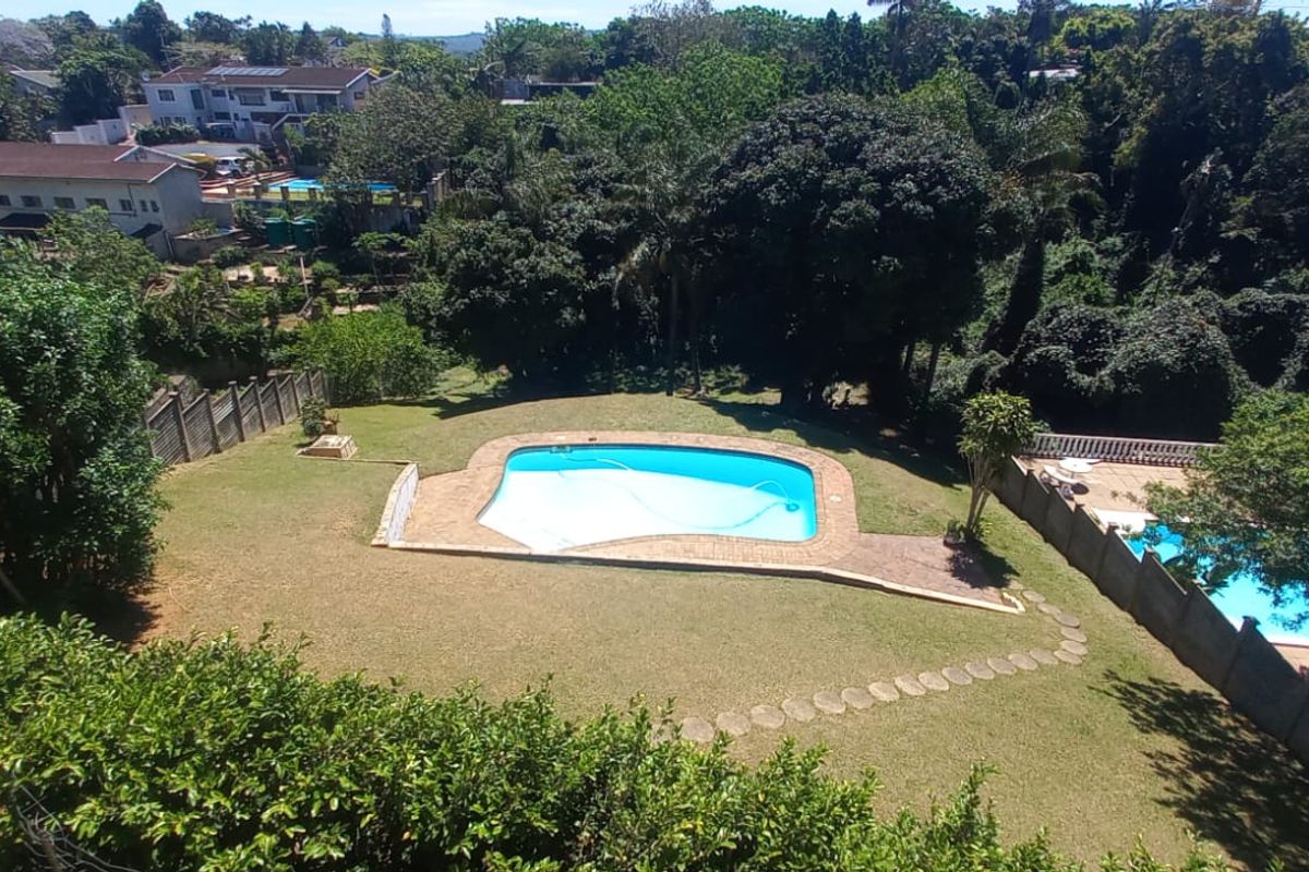 Aerial view of a residential property featuring a swimming pool, expansive lawn, and established garden surroundings.