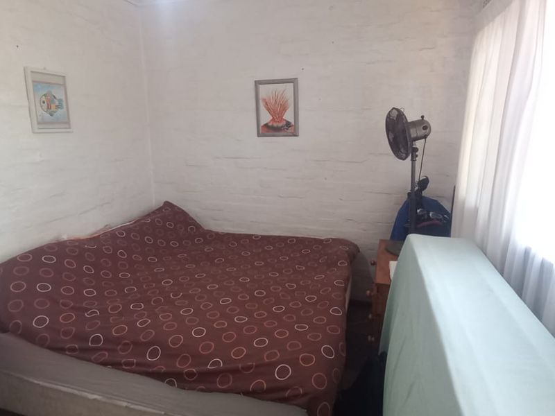 A compact bedroom featuring painted brick walls and a window with curtains, offering a simple and functional living space.