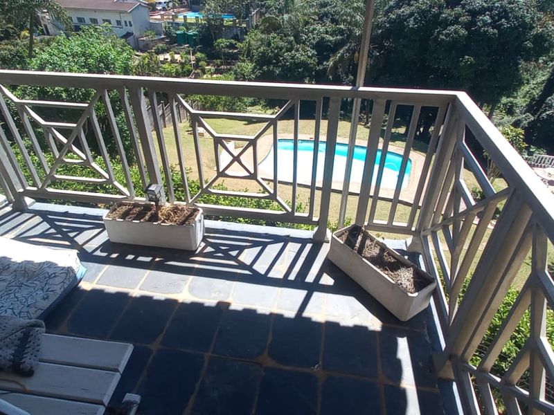 A balcony featuring tiled flooring and a decorative railing, offering an elevated view of the garden and swimming pool area below.