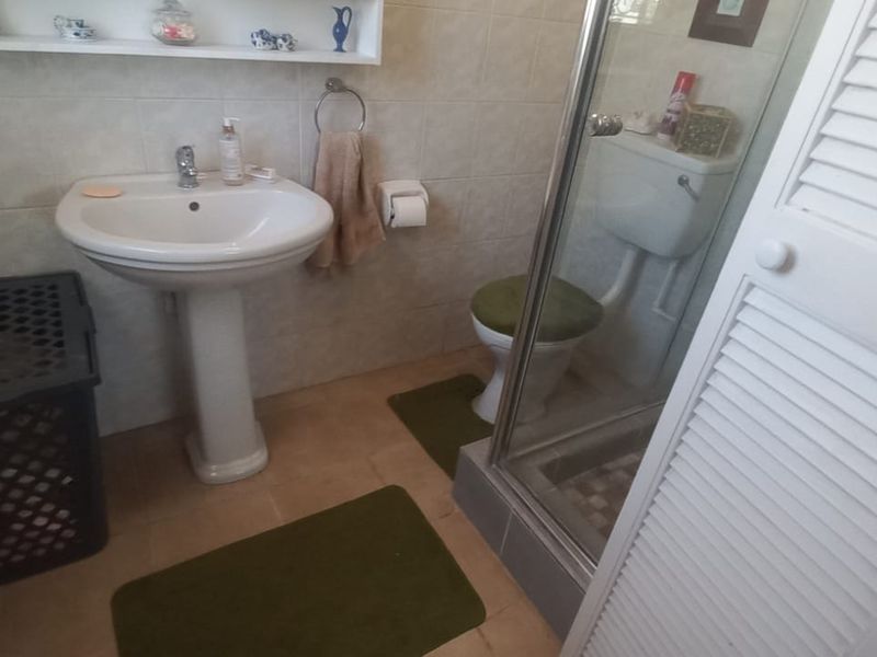 A functional bathroom featuring a pedestal basin, a glass-enclosed shower, and a toilet, finished with neutral wall and floor tiling.