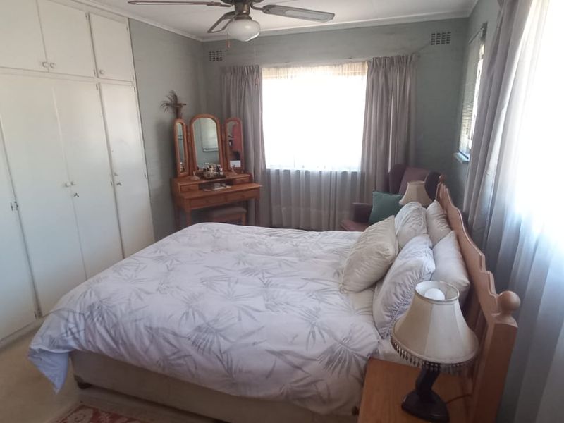 A functional bedroom featuring extensive built-in cupboard storage and a ceiling fan, offering a neutral canvas for potential updates.