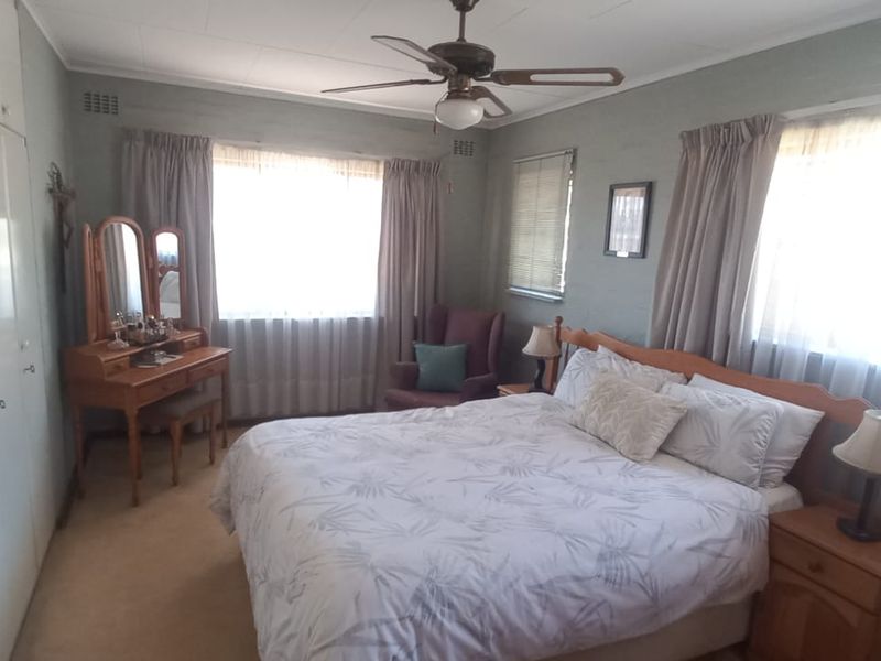 A spacious bedroom featuring built-in cupboards, a ceiling fan, and large windows that provide ample natural light.