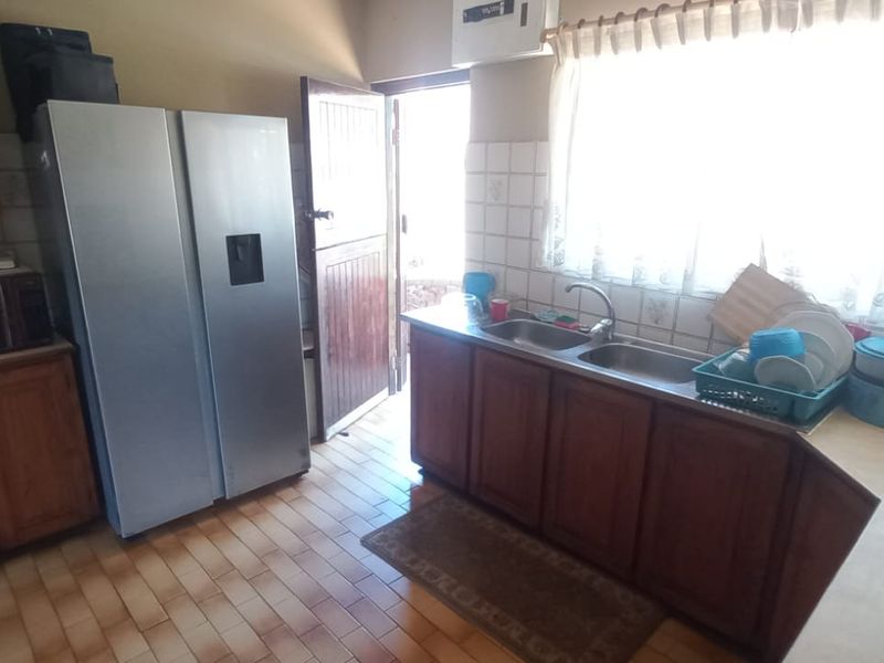 A functional kitchen featuring wooden cabinetry, a double basin sink, tiled backsplash, and direct access to the exterior via a stable door.